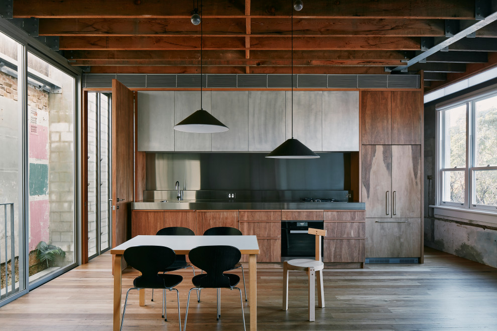Idéer för att renovera ett industriellt grå linjärt grått kök, med en integrerad diskho, släta luckor, skåp i mellenmörkt trä, bänkskiva i rostfritt stål, integrerade vitvaror, mellanmörkt trägolv och brunt golv