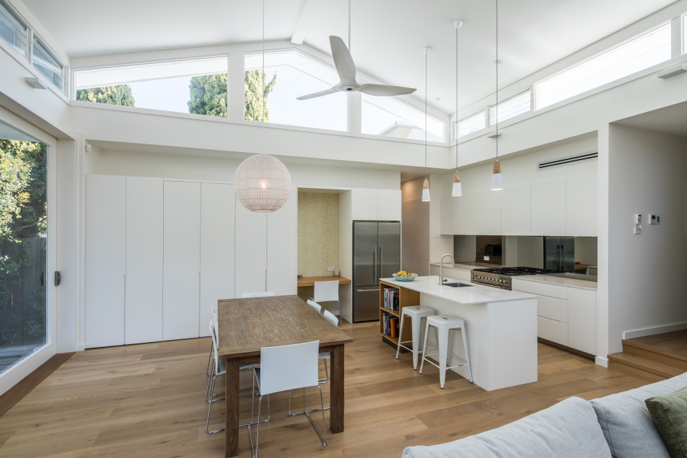 Contemporary eat-in kitchen in Sydney with an undermount sink, white cabinets, quartz benchtops, grey splashback, glass sheet splashback, stainless steel appliances, light hardwood floors, with island, brown floor and white benchtop.