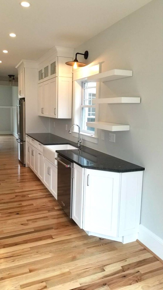 Expansive beach style l-shaped eat-in kitchen in Baltimore with a single-bowl sink, shaker cabinets, white cabinets, granite benchtops, stainless steel appliances, light hardwood floors, with island, brown floor and white benchtop.