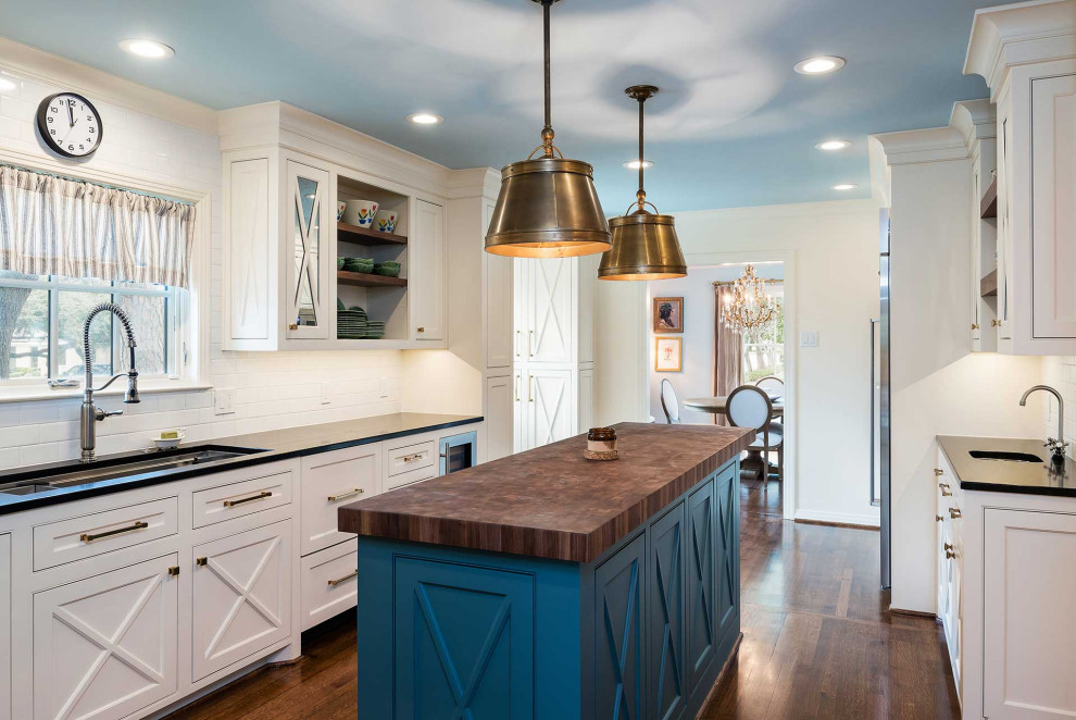 Design ideas for a large traditional l-shaped separate kitchen in Dallas with recessed-panel cabinets, white cabinets, quartz benchtops, white splashback, ceramic splashback, stainless steel appliances, medium hardwood floors, with island, brown floor and black benchtop.