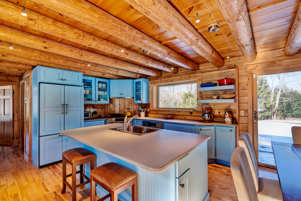 This is an example of a mid-sized country l-shaped open plan kitchen in Burlington with shaker cabinets, blue cabinets, solid surface benchtops, with island, grey benchtop, a single-bowl sink, timber splashback, medium hardwood floors and panelled appliances.