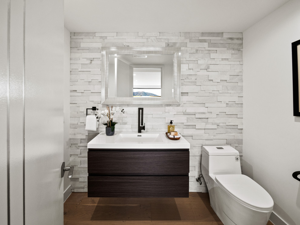 Photo of a contemporary powder room in Los Angeles with flat-panel cabinets, dark wood cabinets, a one-piece toilet, gray tile, stone tile, white walls, medium hardwood floors, an integrated sink, brown floor, white benchtops and a floating vanity.