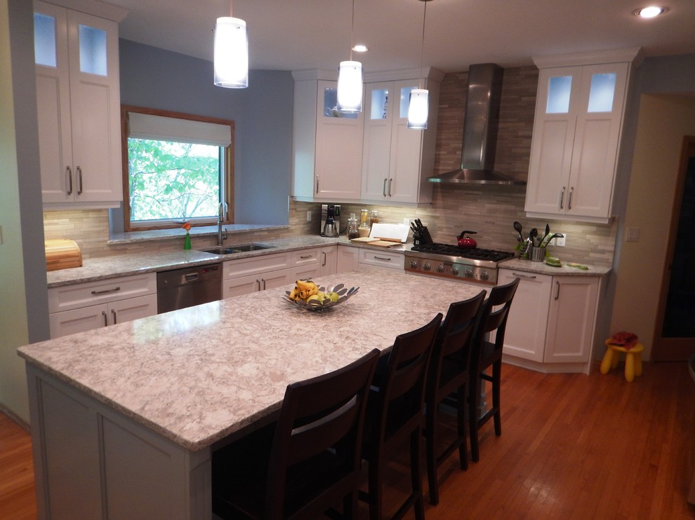 Inspiration for a large transitional l-shaped light wood floor eat-in kitchen remodel with an undermount sink, recessed-panel cabinets, white cabinets, quartz countertops, gray backsplash, stone tile backsplash, stainless steel appliances and an island