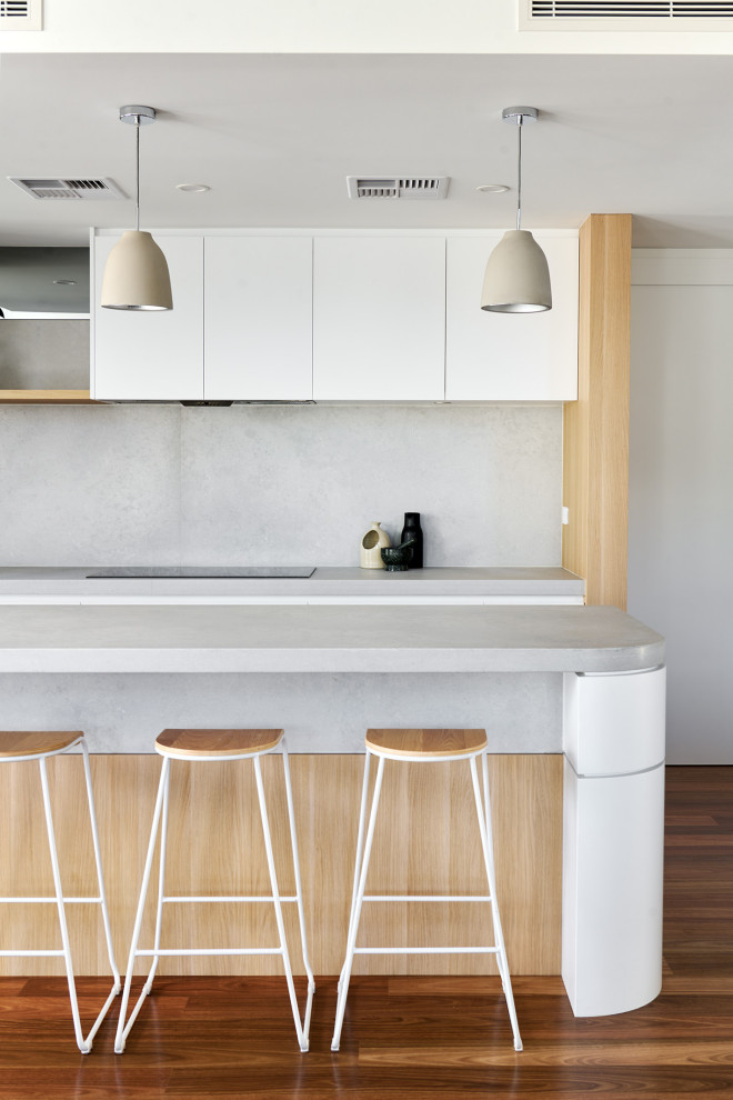Large scandinavian l-shaped eat-in kitchen in Perth with a double-bowl sink, flat-panel cabinets, white cabinets, quartz benchtops, grey splashback, engineered quartz splashback, black appliances, medium hardwood floors, with island, brown floor and grey benchtop.