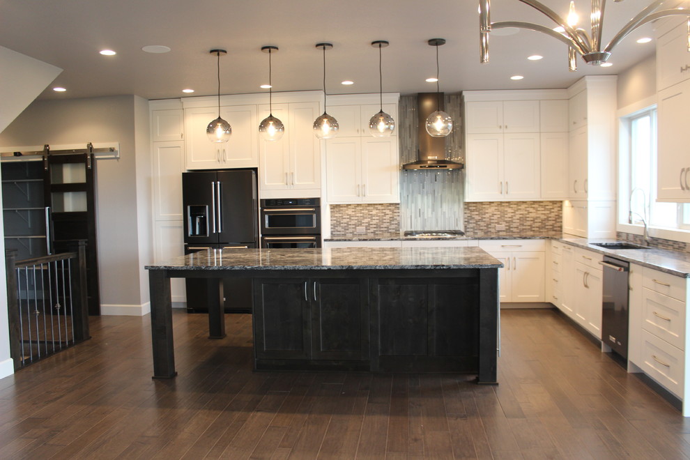 Example of a large transitional l-shaped medium tone wood floor and brown floor kitchen design with an undermount sink, shaker cabinets, white cabinets, granite countertops, multicolored backsplash, mosaic tile backsplash, black appliances and an island