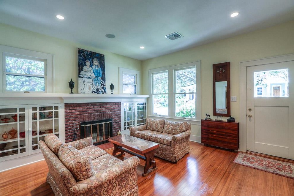 Mid-sized arts and crafts enclosed living room in Houston with yellow walls, medium hardwood floors, a standard fireplace, a brick fireplace surround and a built-in media wall.