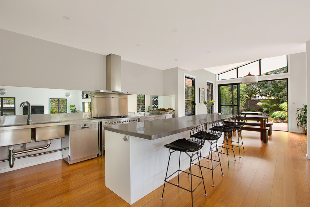 Inspiration for a large industrial single-wall eat-in kitchen in Sydney with with island, a double-bowl sink, stainless steel cabinets, stainless steel benchtops, mirror splashback, stainless steel appliances and bamboo floors.