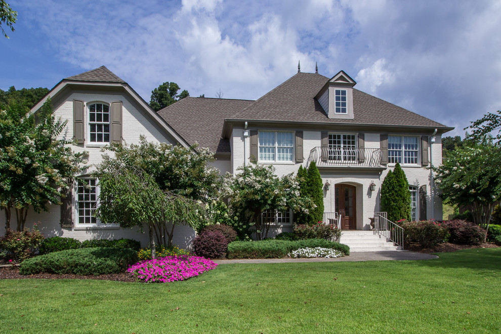 Mid-sized traditional two-storey brick white house exterior in Other with a clipped gable roof and a shingle roof.