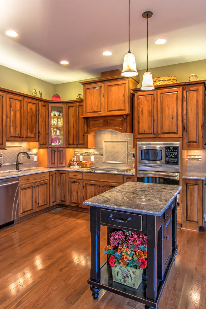 Example of a mountain style kitchen design with raised-panel cabinets, granite countertops, subway tile backsplash and an island