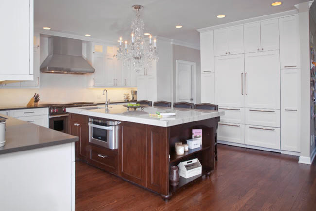 Mid-sized transitional l-shaped eat-in kitchen in Chicago with a farmhouse sink, recessed-panel cabinets, white cabinets, marble benchtops, white splashback, mosaic tile splashback, stainless steel appliances, medium hardwood floors and with island.