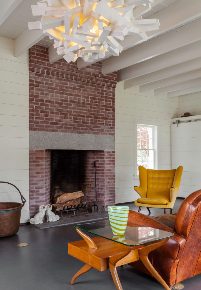 Photo of a country living room in New York with white walls, concrete floors, a standard fireplace, a brick fireplace surround and grey floor.