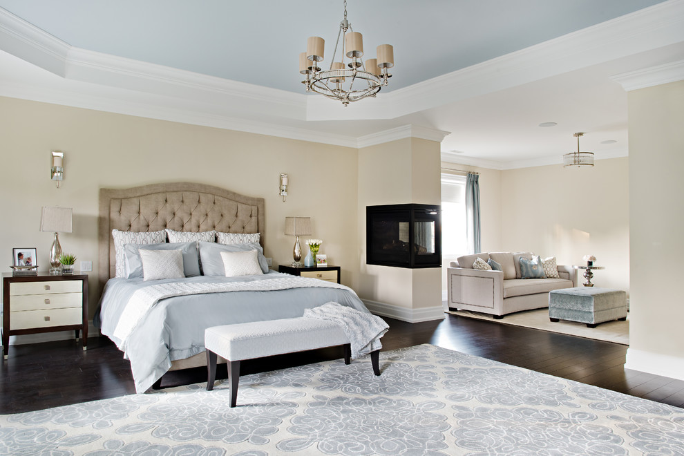 Design ideas for an expansive transitional master bedroom in Toronto with beige walls, dark hardwood floors, a two-sided fireplace and a metal fireplace surround.