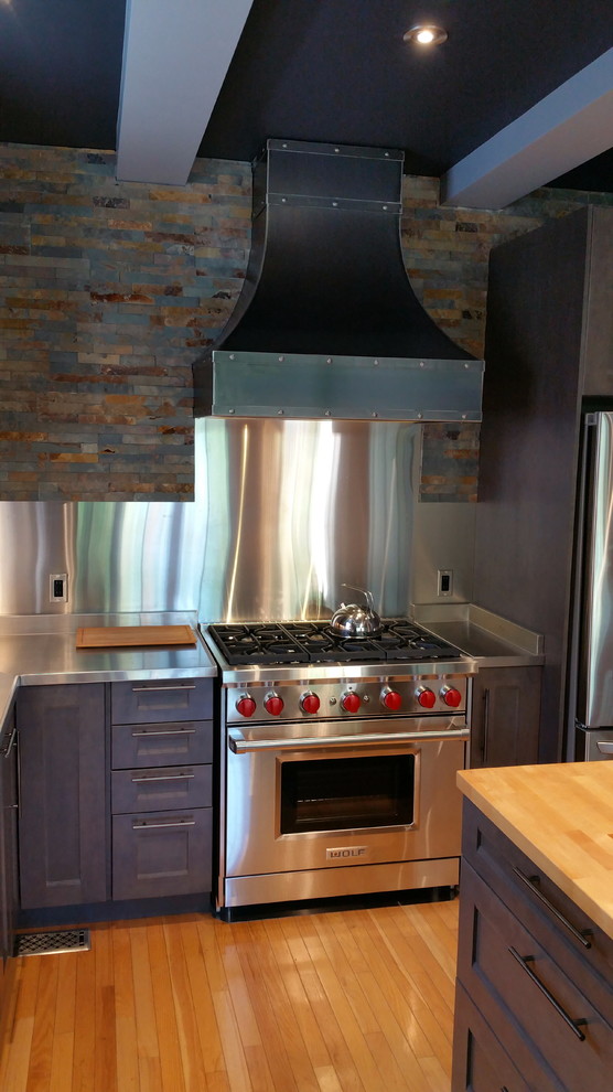 Inspiration for a mid-sized industrial l-shaped separate kitchen in Ottawa with a double-bowl sink, shaker cabinets, grey cabinets, stainless steel benchtops, metallic splashback, stone tile splashback, stainless steel appliances, light hardwood floors and with island.