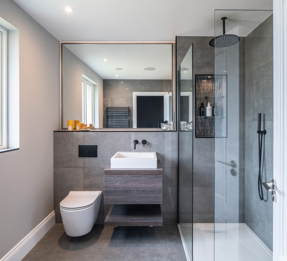 Idéer för att renovera ett funkis brun brunt badrum med dusch, med släta luckor, skåp i mörkt trä, en hörndusch, en vägghängd toalettstol, grå kakel, grå väggar, ett fristående handfat, träbänkskiva, grått golv och med dusch som är öppen