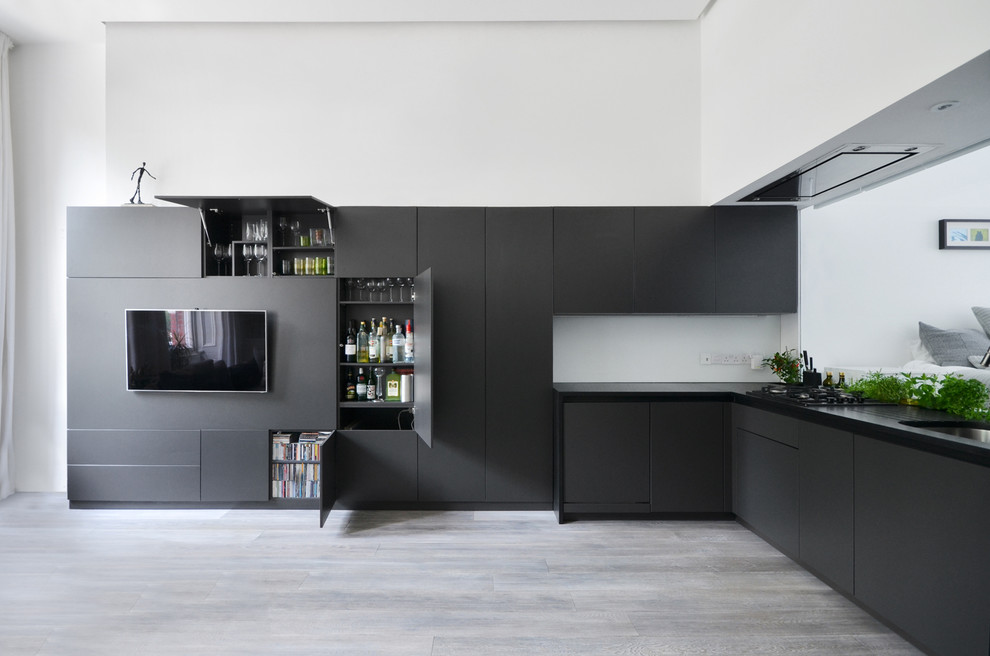Small contemporary l-shaped open plan kitchen in London with a double-bowl sink, flat-panel cabinets, black cabinets, light hardwood floors, no island, grey floor and black benchtop.
