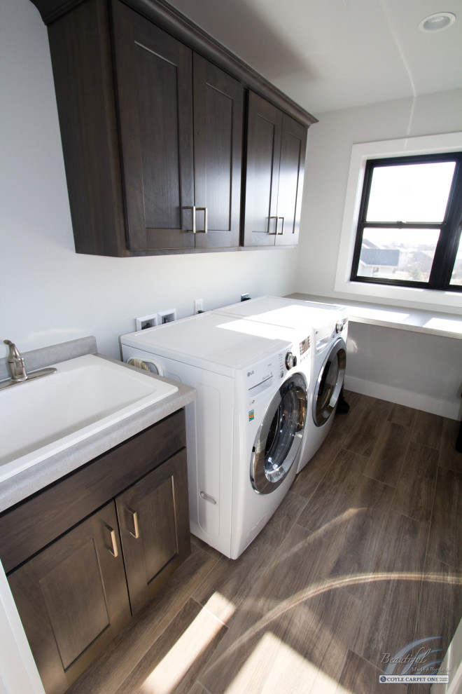 Mid-sized transitional l-shaped dedicated laundry room in Other with an utility sink, recessed-panel cabinets, medium wood cabinets, laminate benchtops, white walls, porcelain floors, a side-by-side washer and dryer, brown floor and grey benchtop.