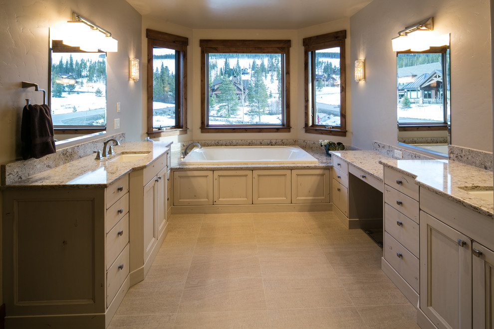Inspiration for a mid-sized country master bathroom in Denver with recessed-panel cabinets, distressed cabinets, a drop-in tub, a corner shower, beige walls, an undermount sink and granite benchtops.