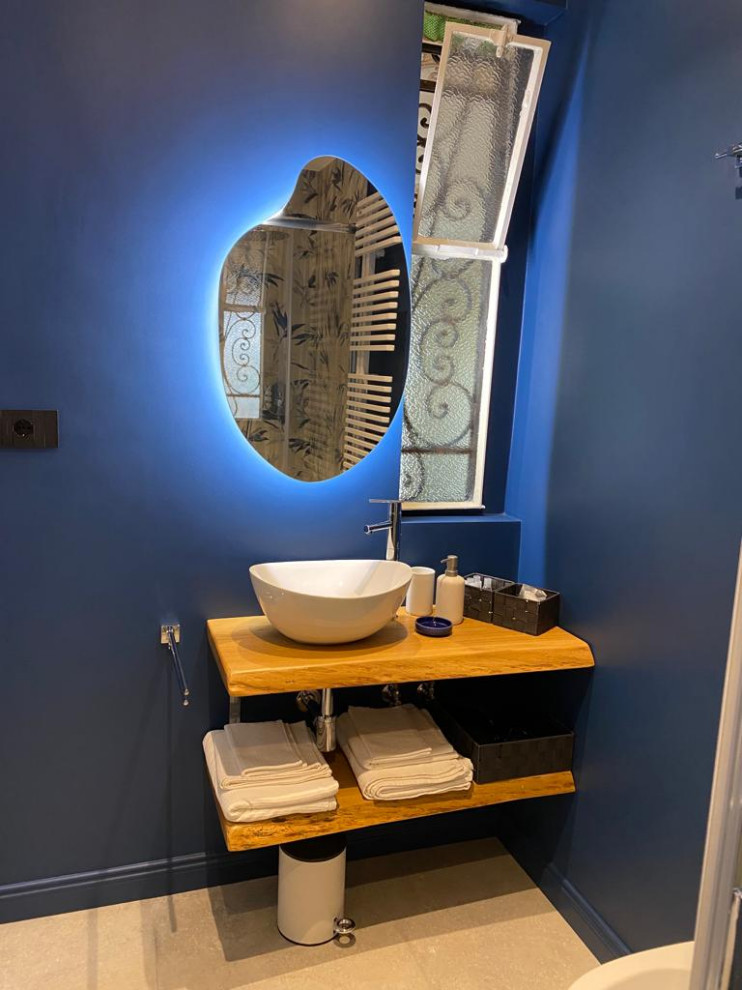 Eklektisk inredning av ett litet brun brunt toalett, med öppna hyllor, skåp i ljust trä, en toalettstol med separat cisternkåpa, blå väggar, klinkergolv i porslin, ett fristående handfat, träbänkskiva och grått golv