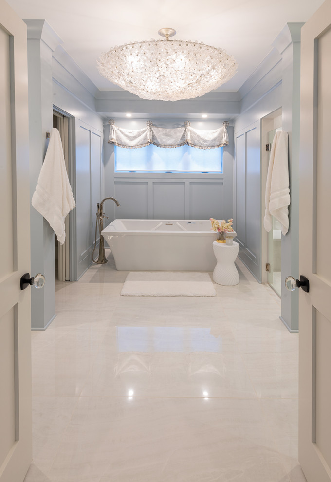 Photo of a large modern master bathroom in New York with recessed-panel cabinets, blue cabinets, a freestanding tub, blue walls, travertine floors, marble benchtops, beige floor, white benchtops, a double vanity, a built-in vanity and panelled walls.
