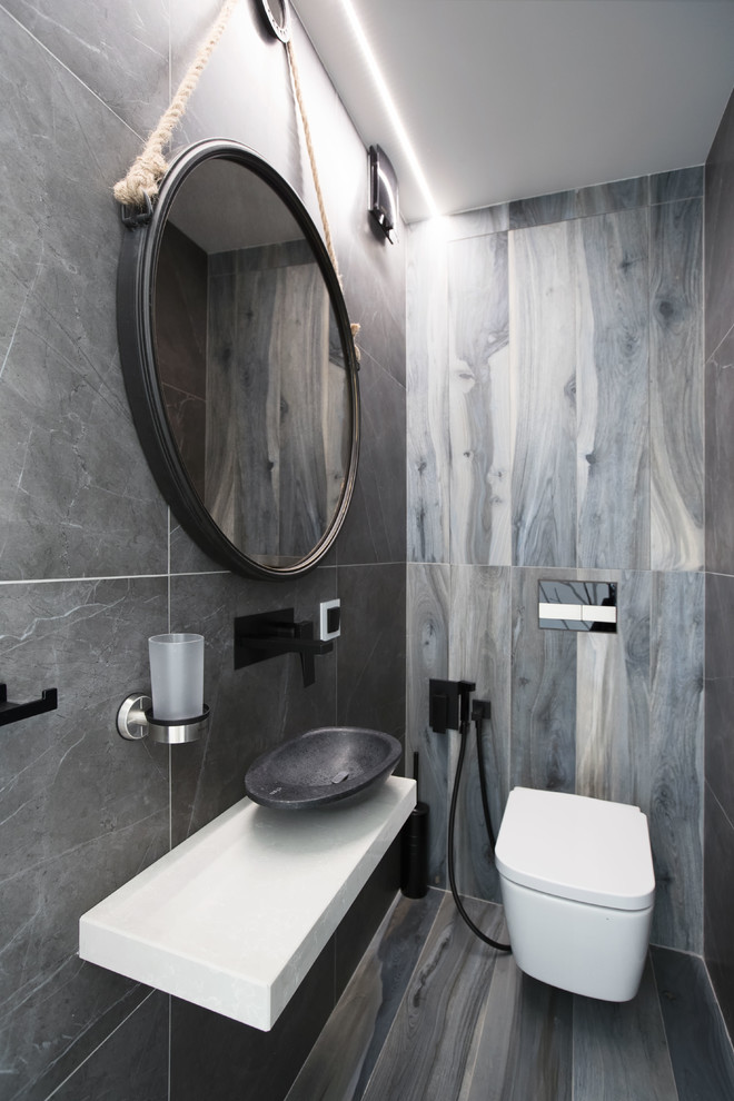 This is an example of a contemporary powder room in Moscow with a wall-mount toilet, gray tile, a vessel sink and grey floor.