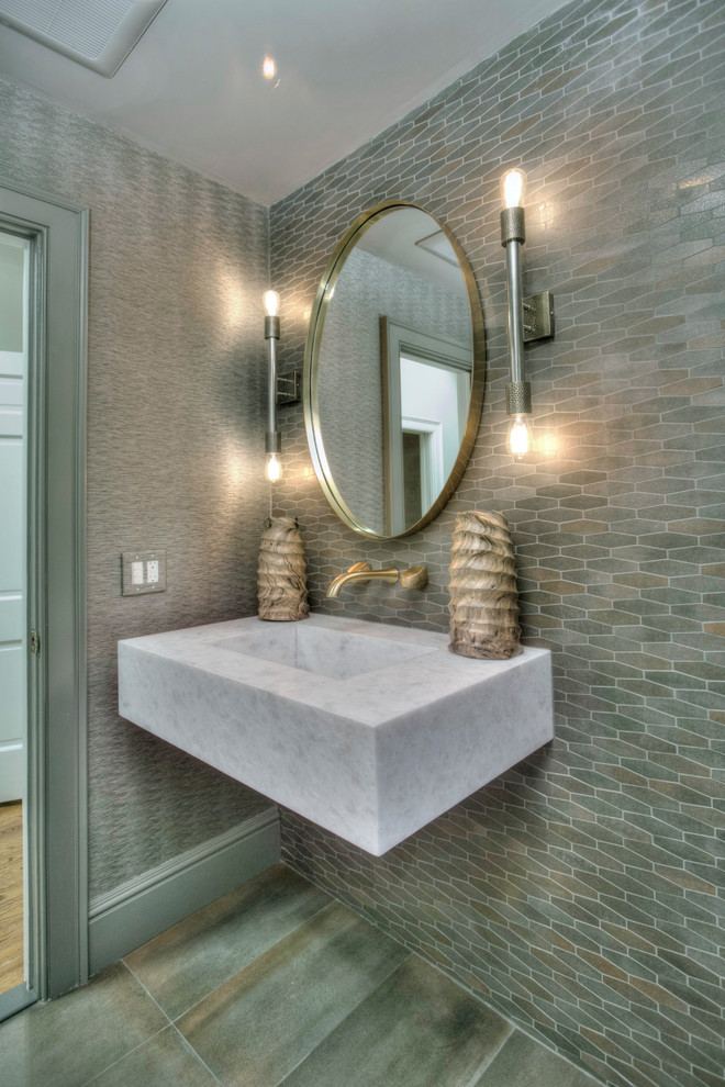 Inspiration for a mid-sized transitional powder room in New York with a one-piece toilet, gray tile, porcelain tile, grey walls, porcelain floors, a wall-mount sink, marble benchtops, grey floor and white benchtops.