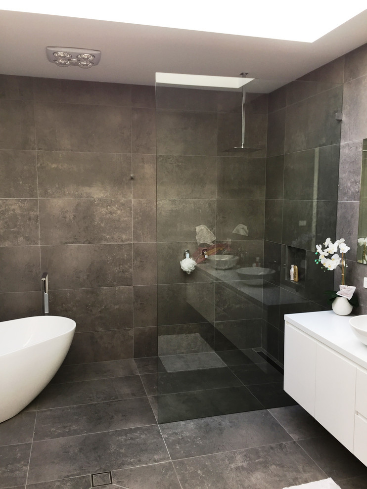 This is an example of a small modern master bathroom in Sydney with white cabinets, a freestanding tub, a double shower, a wall-mount toilet, gray tile, slate, grey walls, slate floors, a drop-in sink, grey floor, an open shower and white benchtops.