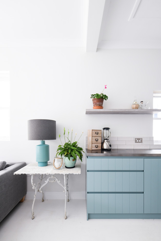Photo of a small beach style l-shaped eat-in kitchen in Sydney with an undermount sink, blue cabinets, stainless steel benchtops, white splashback, subway tile splashback, stainless steel appliances, light hardwood floors, no island, white floor and grey benchtop.