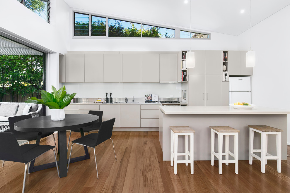 Photo of a mid-sized contemporary galley eat-in kitchen in Sydney with a double-bowl sink, grey cabinets, quartz benchtops, white splashback, glass sheet splashback, stainless steel appliances, medium hardwood floors, with island, white benchtop, flat-panel cabinets and brown floor.