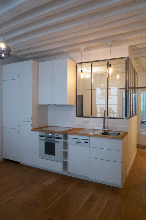 Photo of a small contemporary single-wall open plan kitchen in Paris with a single-bowl sink, beaded inset cabinets, white cabinets, wood benchtops, white splashback, porcelain splashback, white appliances, light hardwood floors and no island.
