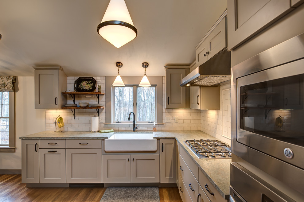 Inspiration for a mid-sized traditional l-shaped kitchen pantry in Boston with a farmhouse sink, recessed-panel cabinets, beige cabinets, granite benchtops, beige splashback, subway tile splashback, stainless steel appliances, medium hardwood floors, no island and brown floor.