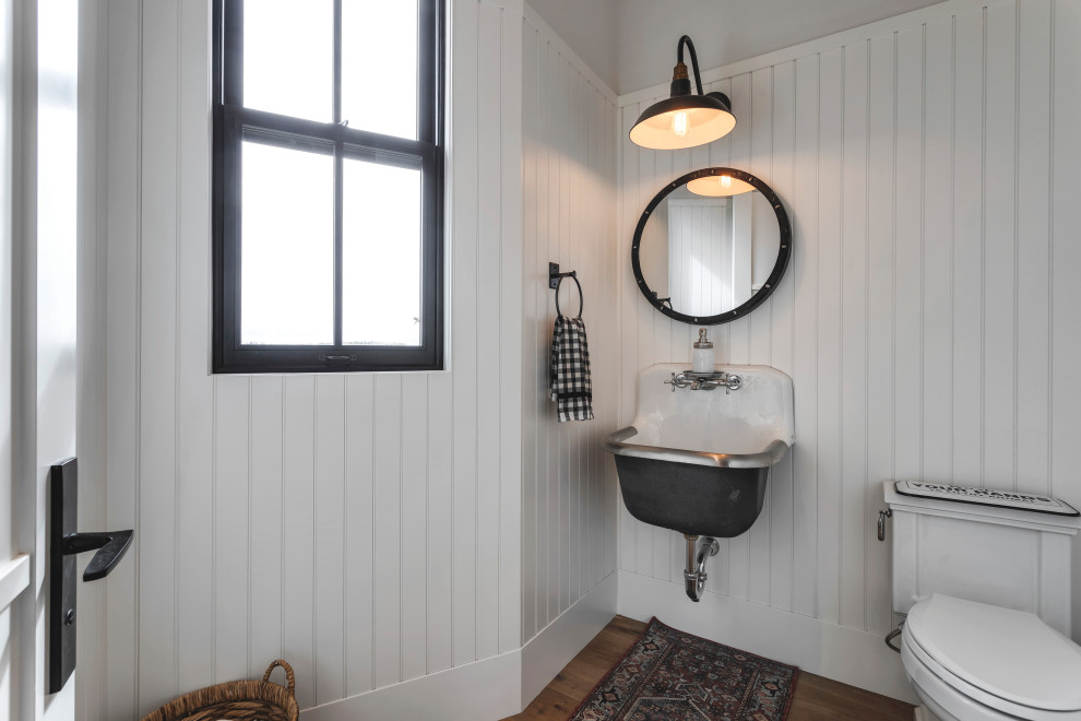 Lantlig inredning av ett stort toalett, med vita väggar, mörkt trägolv, en toalettstol med hel cisternkåpa och ett väggmonterat handfat