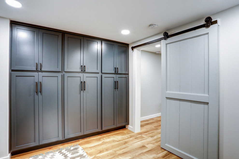 Photo of a large transitional l-shaped dedicated laundry room in Other with a drop-in sink, recessed-panel cabinets, blue cabinets, laminate benchtops, white walls, vinyl floors, a side-by-side washer and dryer, brown floor, grey benchtop and planked wall panelling.
