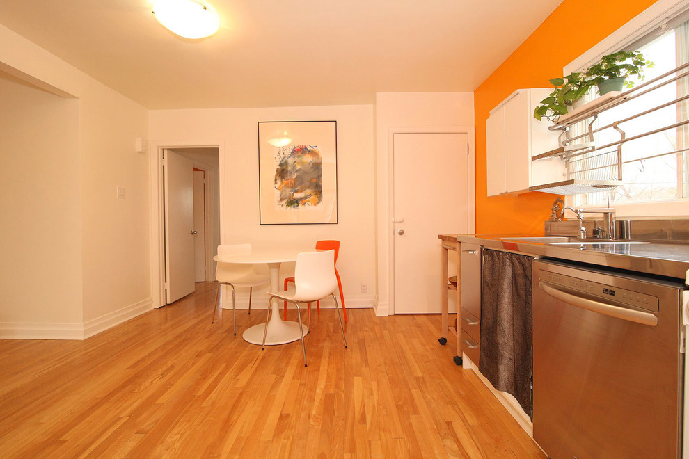 Small asian l-shaped eat-in kitchen in Ottawa with an undermount sink, flat-panel cabinets, white cabinets, stainless steel benchtops, orange splashback, stainless steel appliances, light hardwood floors and no island.