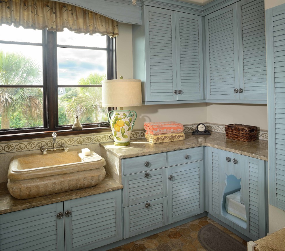 Design ideas for a mid-sized beach style l-shaped laundry room in Charleston with blue cabinets, louvered cabinets, beige walls, a single-bowl sink, limestone benchtops, limestone floors and beige benchtop.