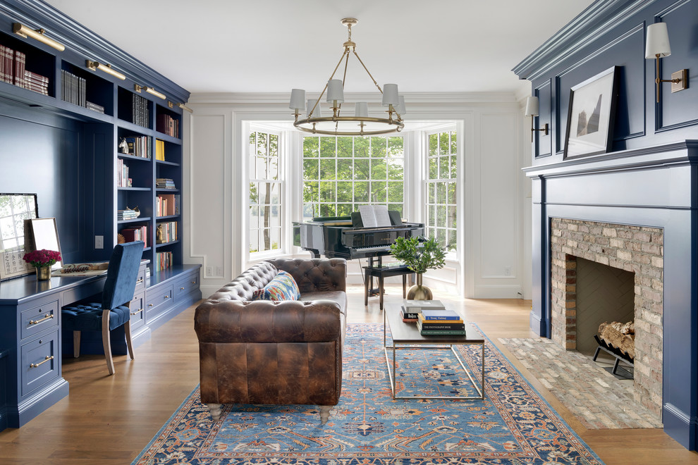 Photo of a beach style home office in Minneapolis with a library, blue walls, a standard fireplace, a brick fireplace surround, a built-in desk and light hardwood floors.
