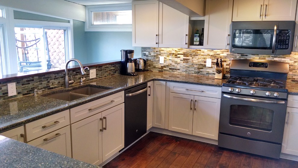 Example of a transitional dark wood floor eat-in kitchen design with an undermount sink, recessed-panel cabinets, white cabinets, quartzite countertops, multicolored backsplash, glass tile backsplash, stainless steel appliances and a peninsula