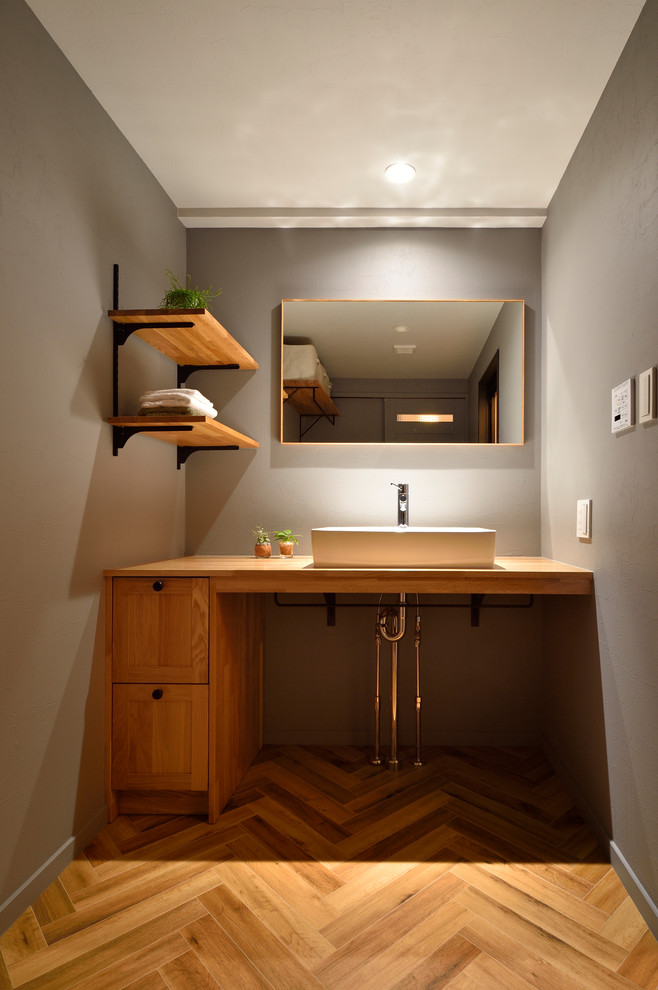 Design ideas for an industrial powder room in Other with recessed-panel cabinets, medium wood cabinets, grey walls, medium hardwood floors, a vessel sink, wood benchtops, brown floor and brown benchtops.