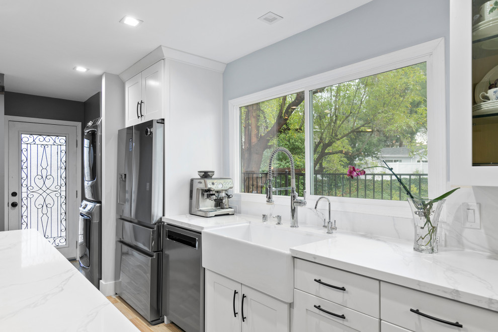 Photo of a mid-sized modern galley eat-in kitchen in Other with a farmhouse sink, shaker cabinets, white cabinets, marble benchtops, white splashback, marble splashback, stainless steel appliances, light hardwood floors, with island, beige floor and white benchtop.