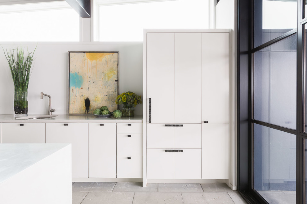 Inspiration for a mid-sized industrial galley open plan kitchen in Other with white benchtop, a drop-in sink, flat-panel cabinets, white cabinets, marble benchtops, white splashback, marble splashback, panelled appliances, travertine floors, with island and beige floor.