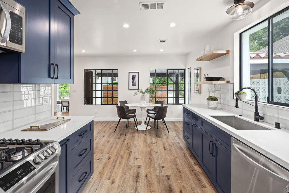 Photo of a large classic galley kitchen/diner in Los Angeles with a submerged sink, shaker cabinets, blue cabinets, engineered stone countertops, white splashback, metro tiled splashback, stainless steel appliances, medium hardwood flooring, no island, brown floors and white worktops.