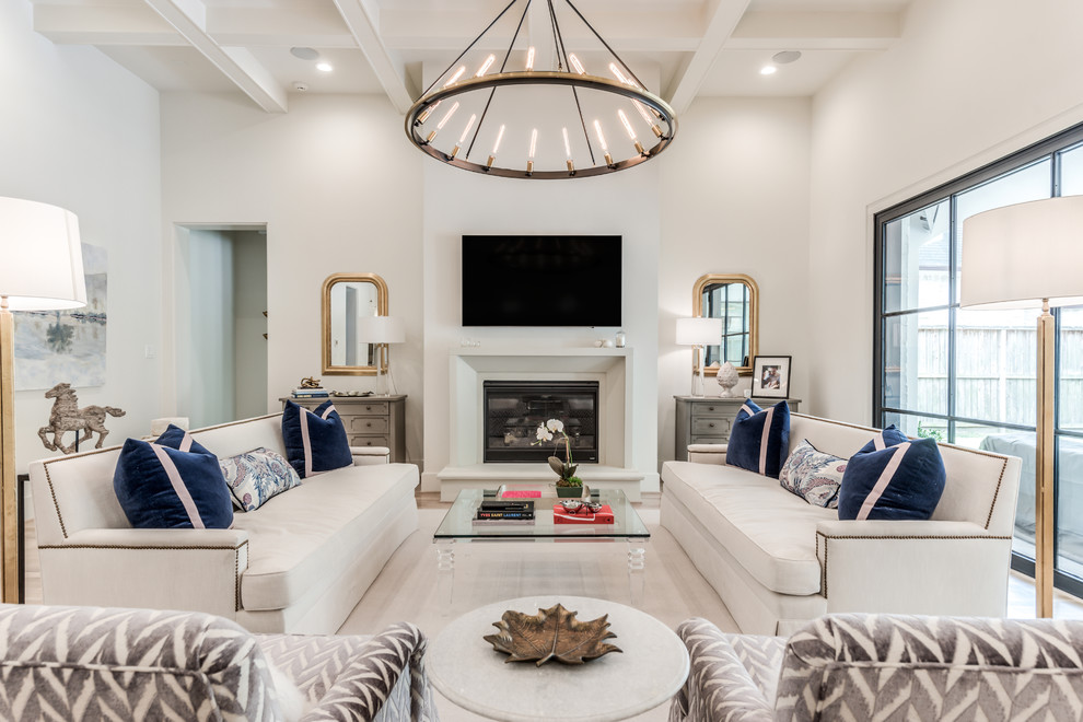 This is an example of an expansive transitional open concept living room in Houston with white walls, light hardwood floors, a standard fireplace, a concrete fireplace surround, a wall-mounted tv and beige floor.