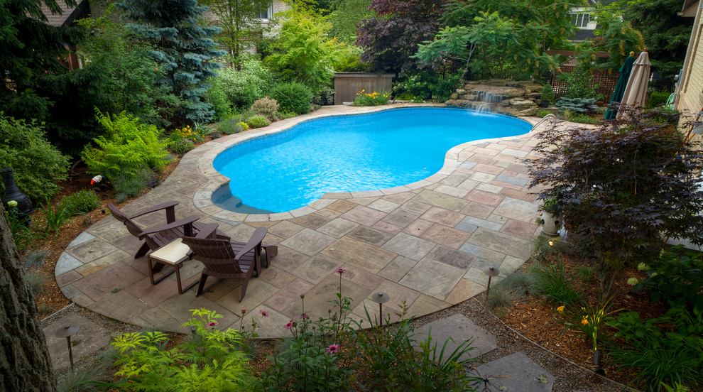Large traditional backyard custom-shaped pool in Toronto with natural stone pavers.