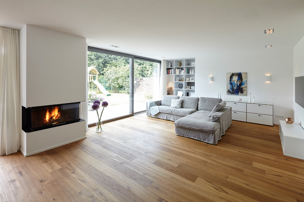 Inspiration for a contemporary open concept living room in Cologne with a library, white walls, medium hardwood floors, a standard fireplace, a plaster fireplace surround, a wall-mounted tv and brown floor.