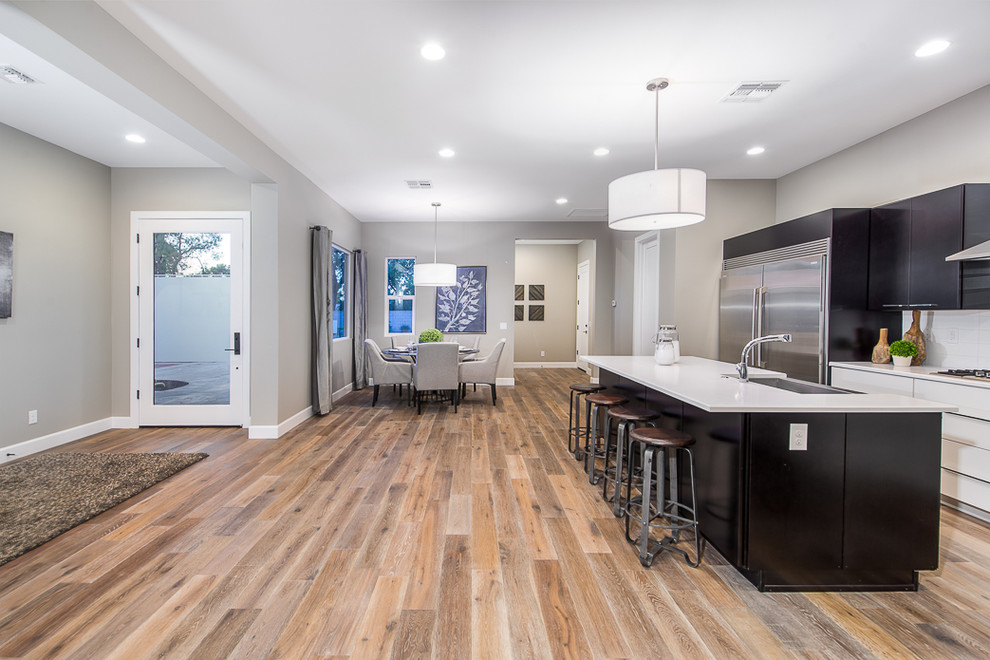 Contemporary u-shaped open plan kitchen in Phoenix with a farmhouse sink, flat-panel cabinets, dark wood cabinets, marble benchtops, white splashback, glass tile splashback, stainless steel appliances, light hardwood floors and with island.