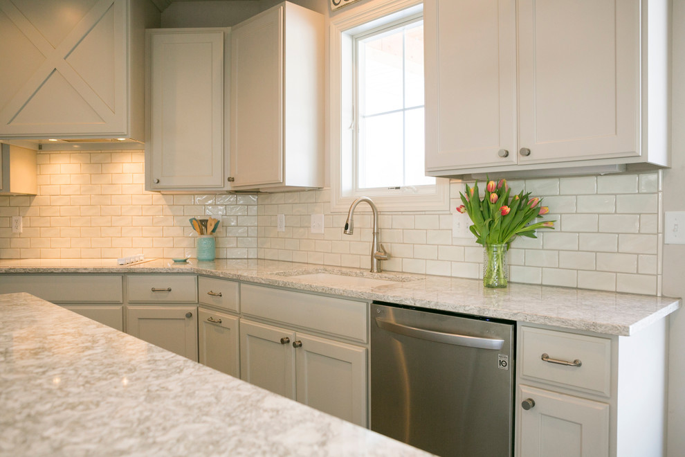 Example of a mid-sized mountain style l-shaped open concept kitchen design with raised-panel cabinets, white cabinets, granite countertops, white backsplash, subway tile backsplash, stainless steel appliances, an island and gray countertops
