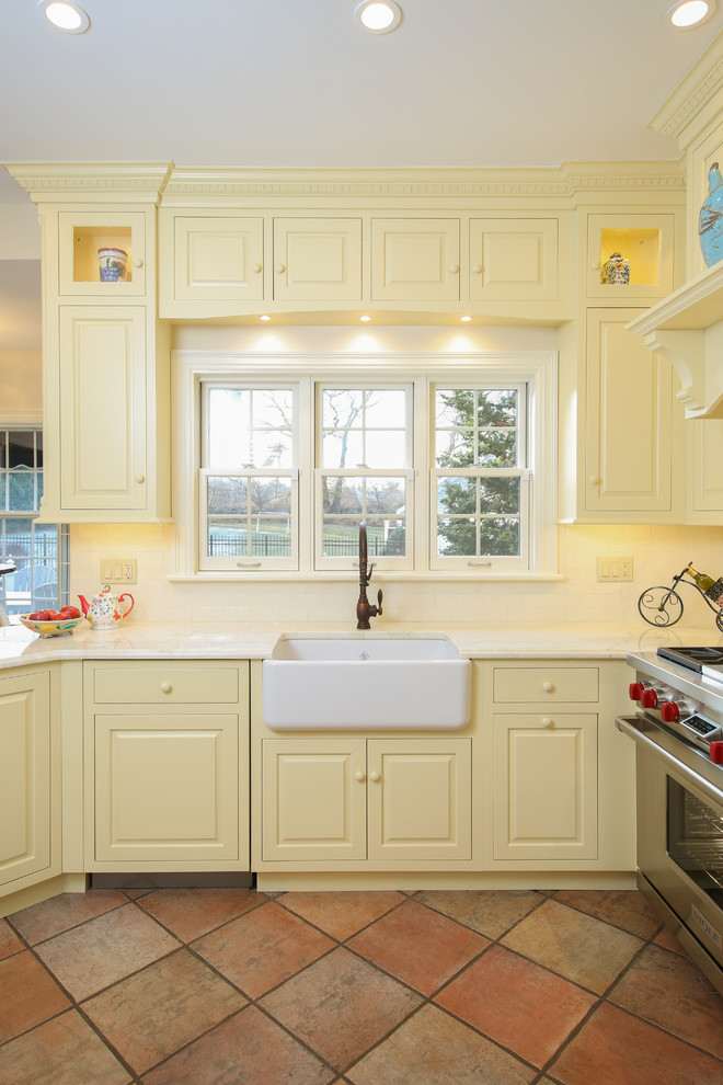 Photo of a mid-sized traditional kitchen in Providence with a farmhouse sink, raised-panel cabinets, yellow cabinets, granite benchtops, white splashback, subway tile splashback, stainless steel appliances, terra-cotta floors, no island and red floor.