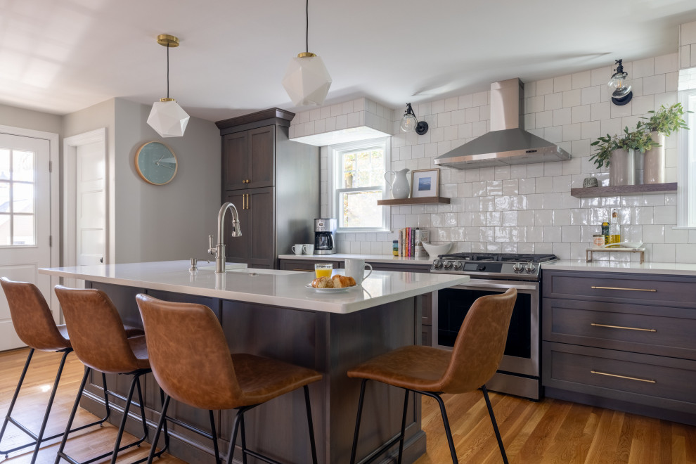 This is an example of a transitional kitchen in Boston with a farmhouse sink, flat-panel cabinets, grey cabinets, quartz benchtops, white splashback, ceramic splashback, stainless steel appliances, medium hardwood floors, with island and white benchtop.