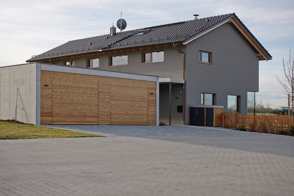 Large contemporary two-storey stucco grey house exterior in Munich with a gable roof and a tile roof.