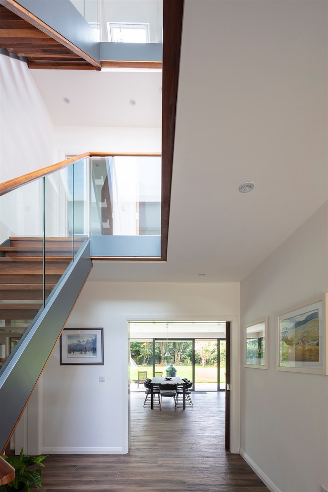 Large modern wood straight staircase in Other with open risers and glass railing.