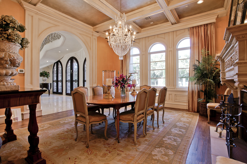 This is an example of a mediterranean dining room in Dallas with orange walls, dark hardwood floors and a standard fireplace.